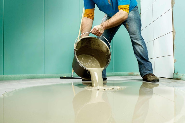 Handwerker giesst Ausgleichsmasse aus Eimer auf Boden