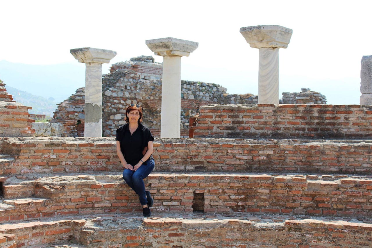 Femme assise sur un escalier en briques devant des ruines de colonnes antiques.