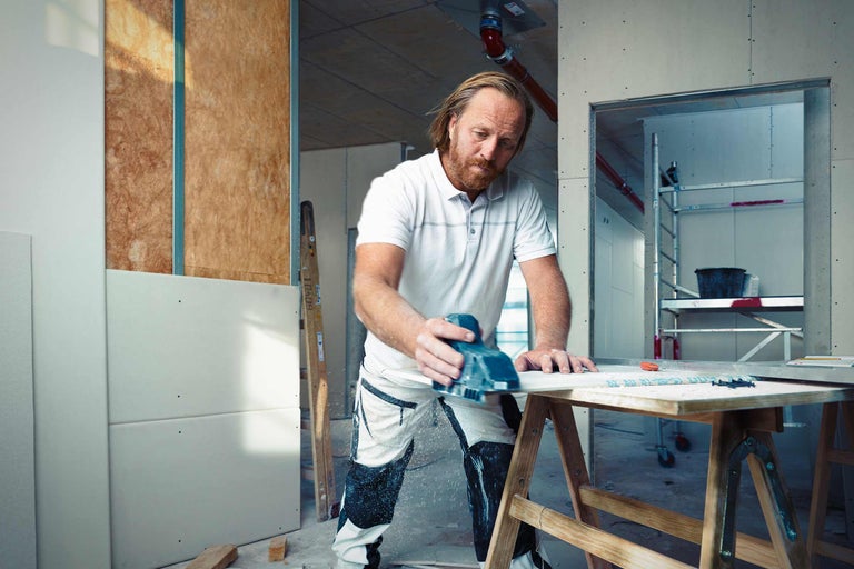 Handwerker schleift Gipskartonplatte auf einer Baustelle