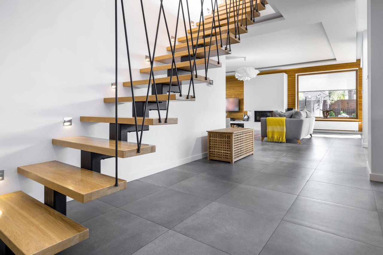 Salon lumineux avec escalier en bois, carrelage gris au sol et mobilier moderne