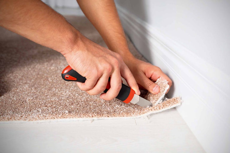 Une personne coupe de la moquette avec un cutter.