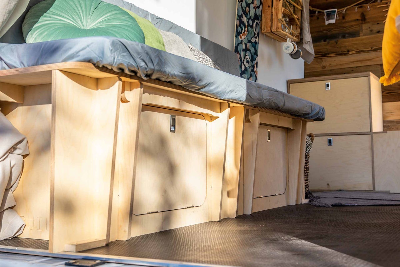 Aménagement intérieur d'un fourgon avec lit, espace de rangement et lambris en bois