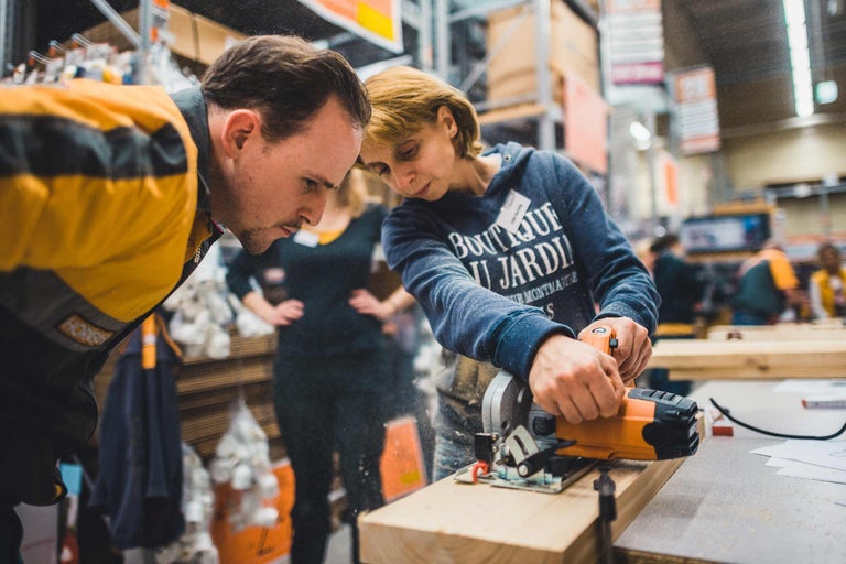Deux personnes travaillent un morceau de bois avec une scie circulaire portative.