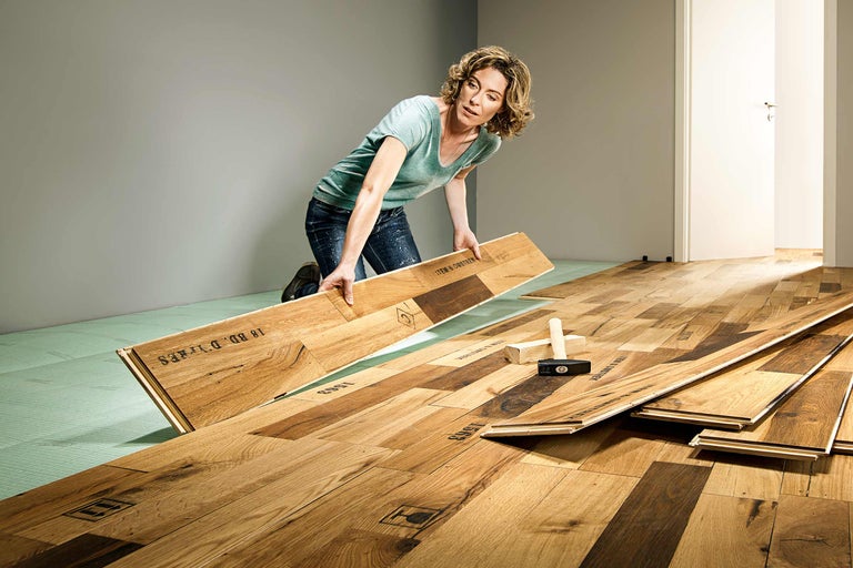 Frau verlegt Holzlaminat auf Dämmunterlage im Innenbereich.