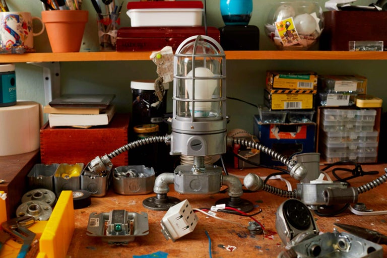 Kreative Werkstattszene mit selbstgebauter Lampe aus Metall und diversen Werkstücken auf einem Holztisch