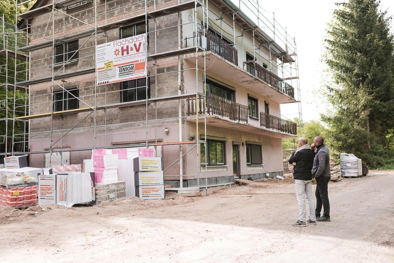 Baustelle mit Gerüst an einem Haus mit Baumaterialien und zwei Personen.