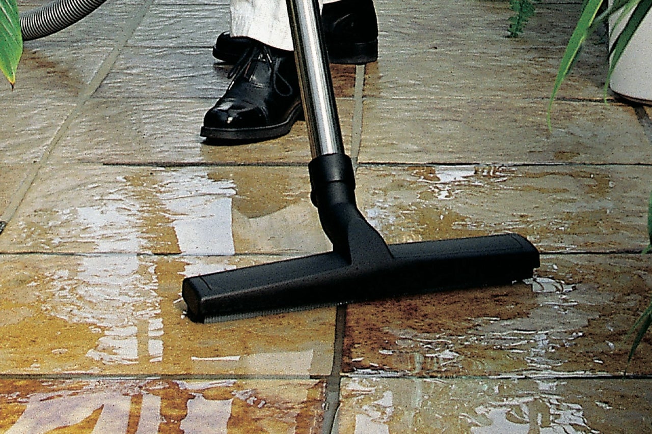 Eine Person benutzt einen Nass Trocken Sauger auf einem gefliesten Boden.