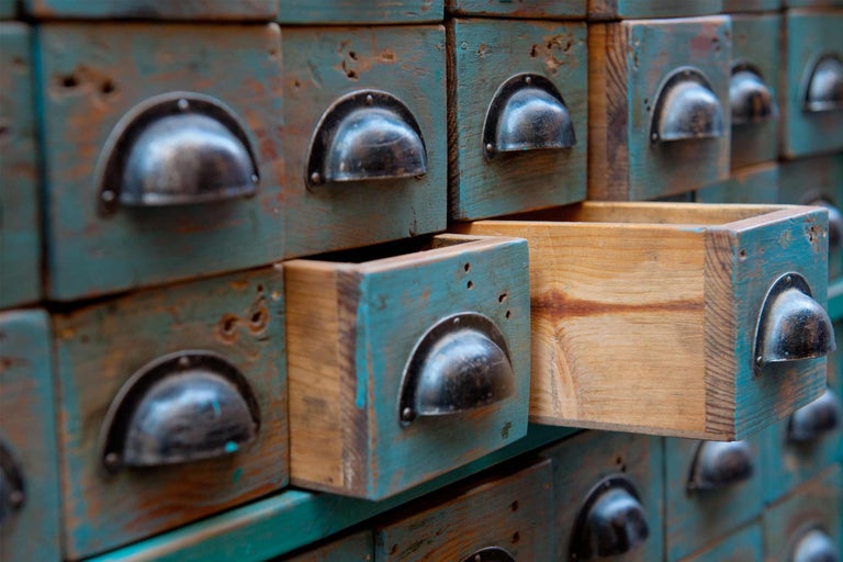 Detailaufnahme eines Apothekerschranks aus Holz mit mehreren Schubladen, wobei eine Schublade geöffnet ist