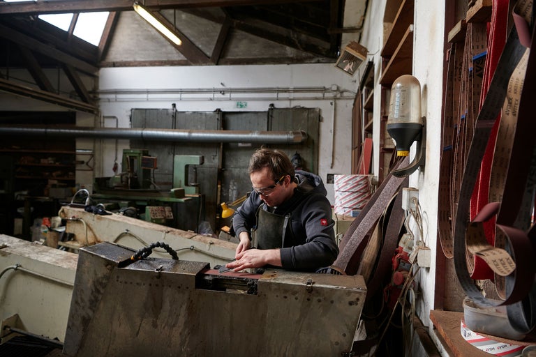 Homme portant des lunettes de sécurité travaillant une pièce métallique sur une rectifieuse, scène d'atelier