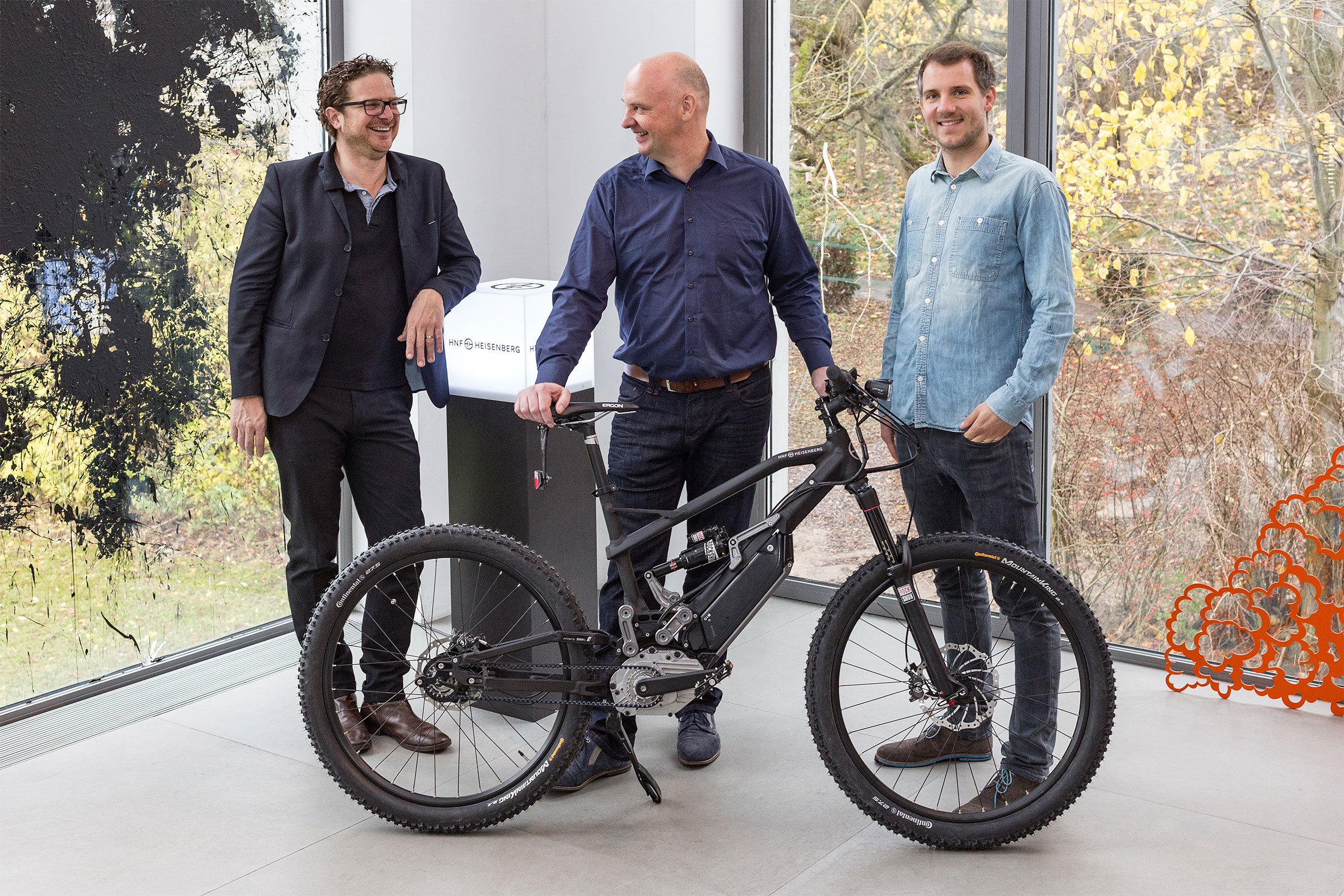 Drei Personen präsentieren ein HNF Heisenberg E-Bike in einem hellen Raum.