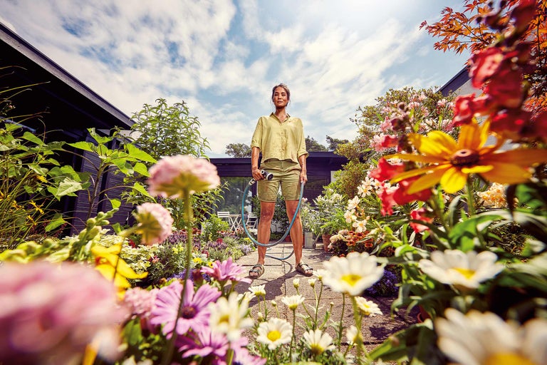 Frau giesst Blumen im Garten mit einem Gartenschlauch.