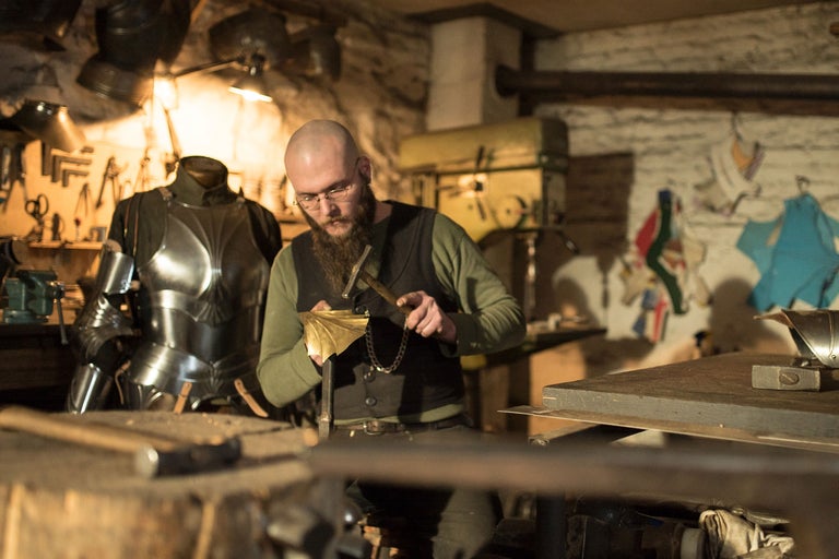 Homme forgeant une pièce métallique dans un atelier avec des outils et une armure