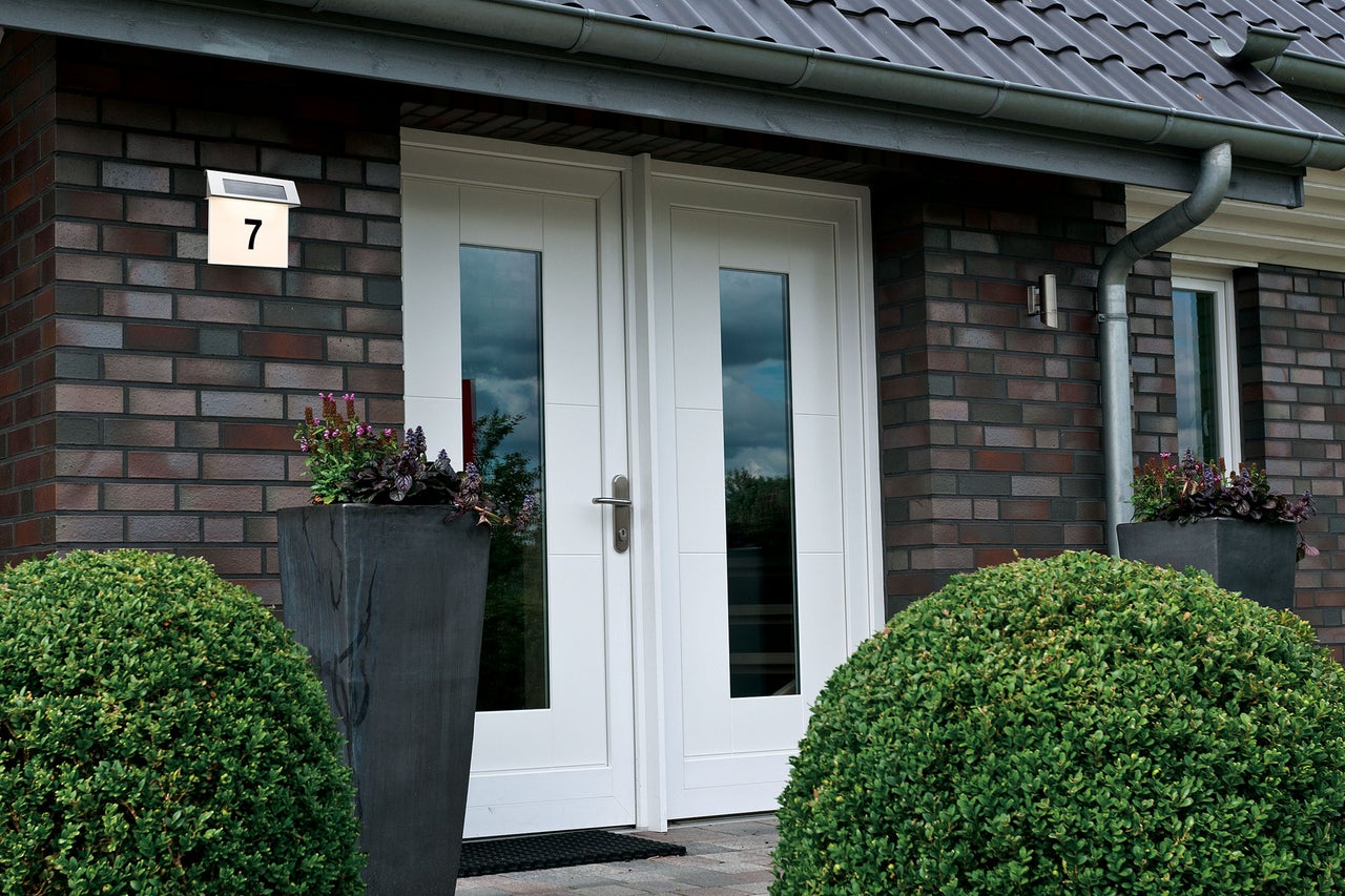 Entrée d'une maison avec double porte d'entrée, numéro de maison lumineux et végétation