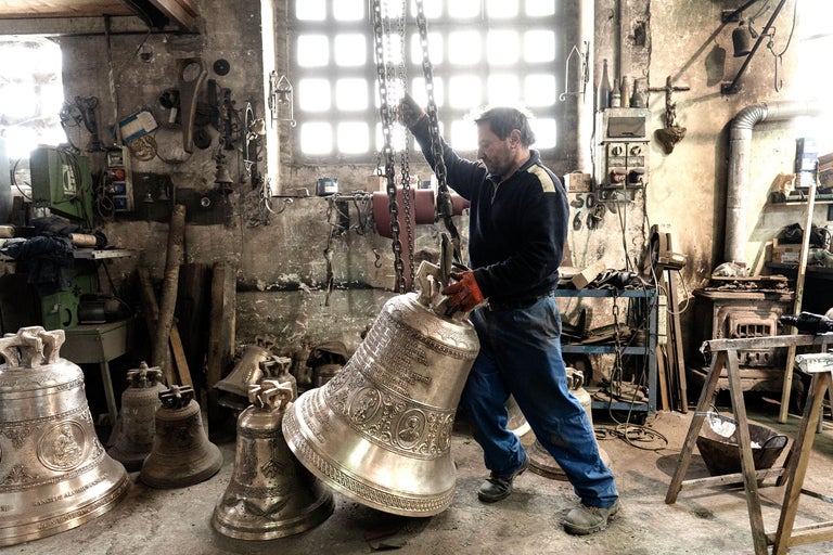 Un artisan dans un atelier manipule une grande cloche sur une chaîne.