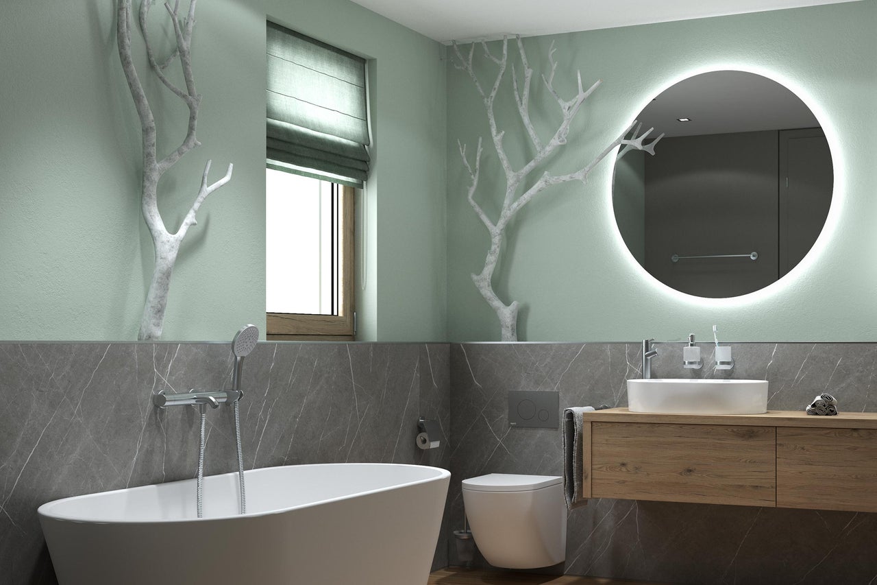 Salle de bains moderne et lumineuse avec baignoire îlot, WC suspendu, meuble en bois, miroir LED rond, murs aspect marbre et décor de branches.