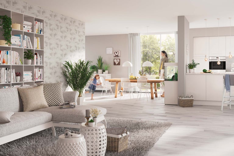Helles Wohnzimmer mit Sofa, Bücherregal, Esstisch und Küche im Hintergrund.