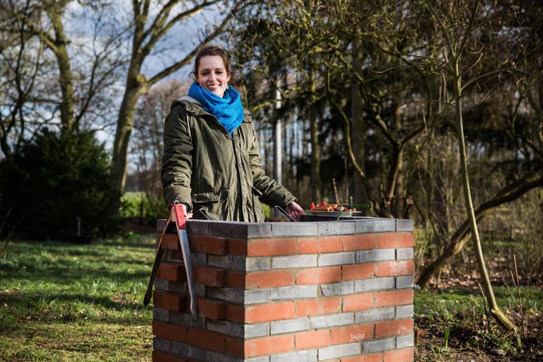 Femme faisant des grillades sur un barbecue en brique dans le jardin