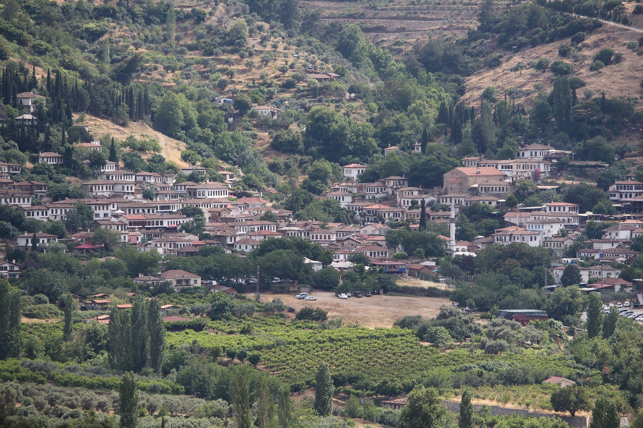 Panorama d'une agglomération avec des maisons d'habitation entourées d'arbres et de collines.
