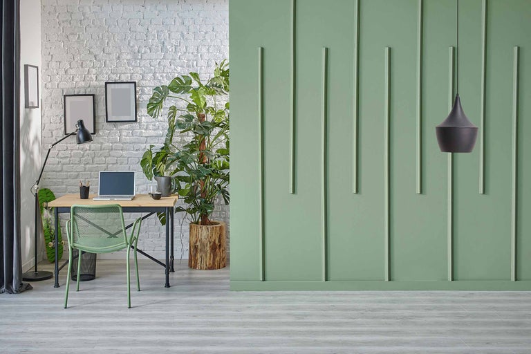 Bureau lumineux avec bureau, chaise et plante d'intérieur devant un mur vert