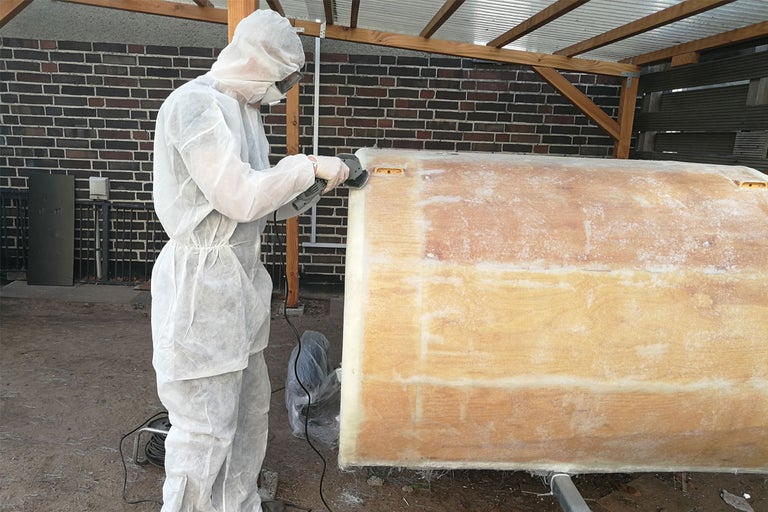Personne en combinaison de protection ponçant une surface avec un outil de ponçage.