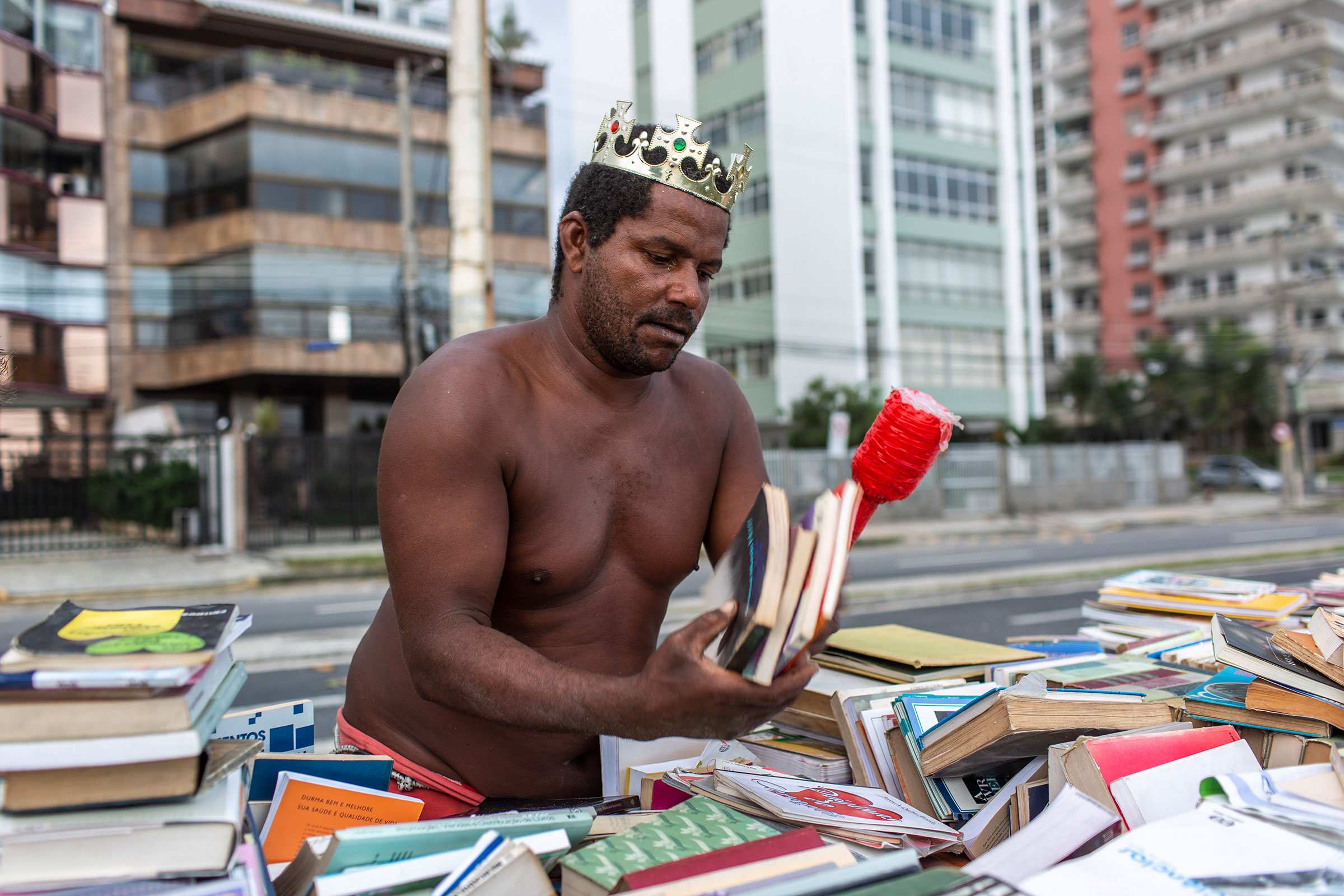 Mann mit Krone sortiert Bücher auf einem Tisch im Freien.