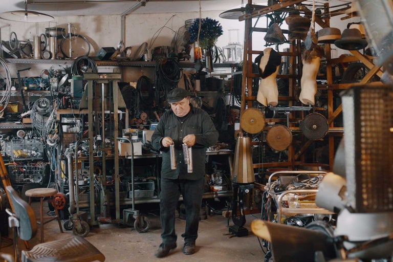 Un homme se tient dans un atelier, entouré d'outils et de divers objets.