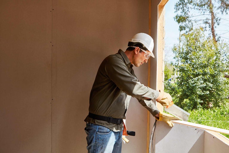 Un ouvrier du bâtiment avec un casque de protection et des lunettes de sécurité travaille sur un cadre de fenêtre sur un chantier.