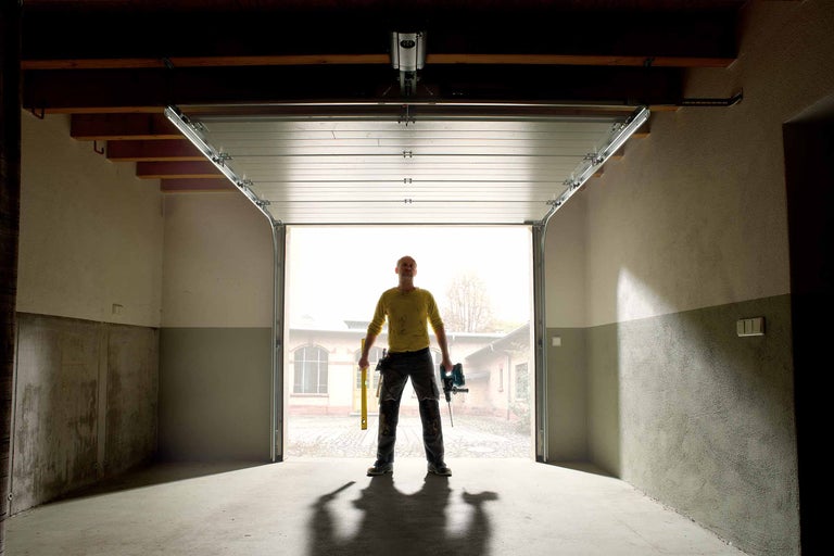 Porte de garage ouverte avec un homme tenant des outils