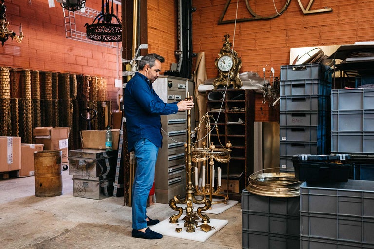 Un homme assemble un chandelier doré dans un entrepôt avec des étagères, des caisses et d'autres objets.