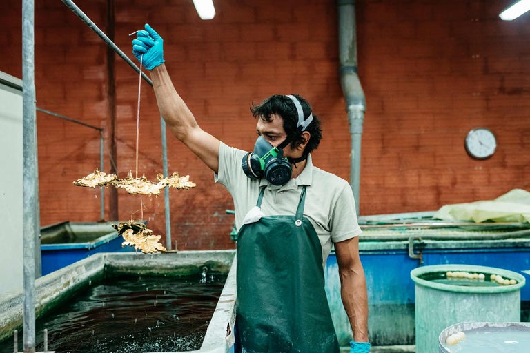 Un ouvrier portant un masque de protection et des gants plonge des ornements dorés dans un bassin d'eau