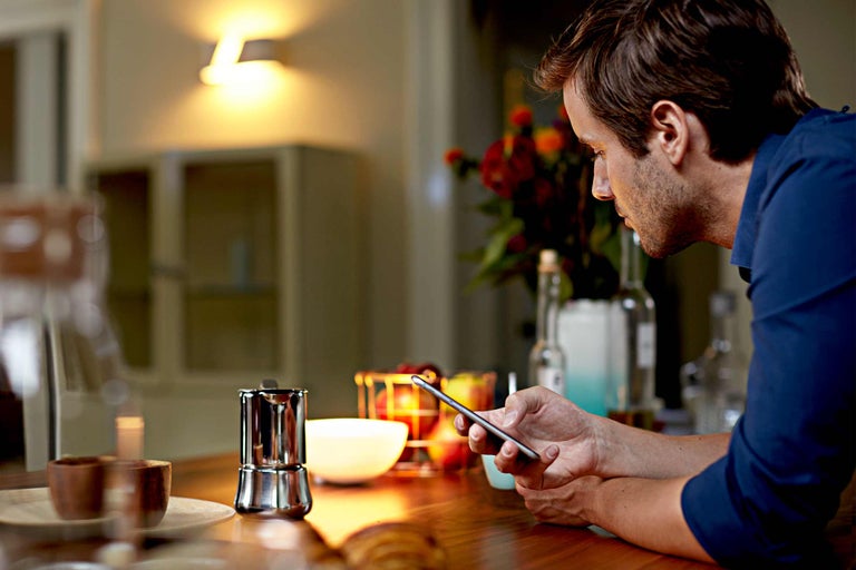 Homme regardant un smartphone sur une table de cuisine avec une cafetière