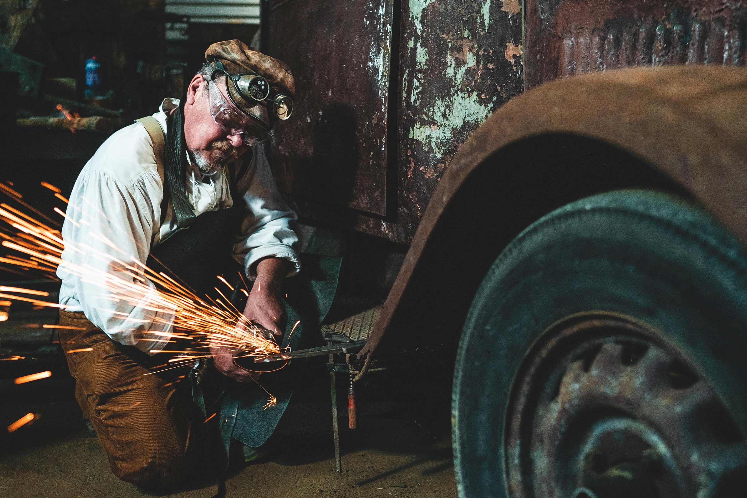 Homme portant des lunettes de protection travaillant sur une voiture ancienne avec une meuleuse d'angle