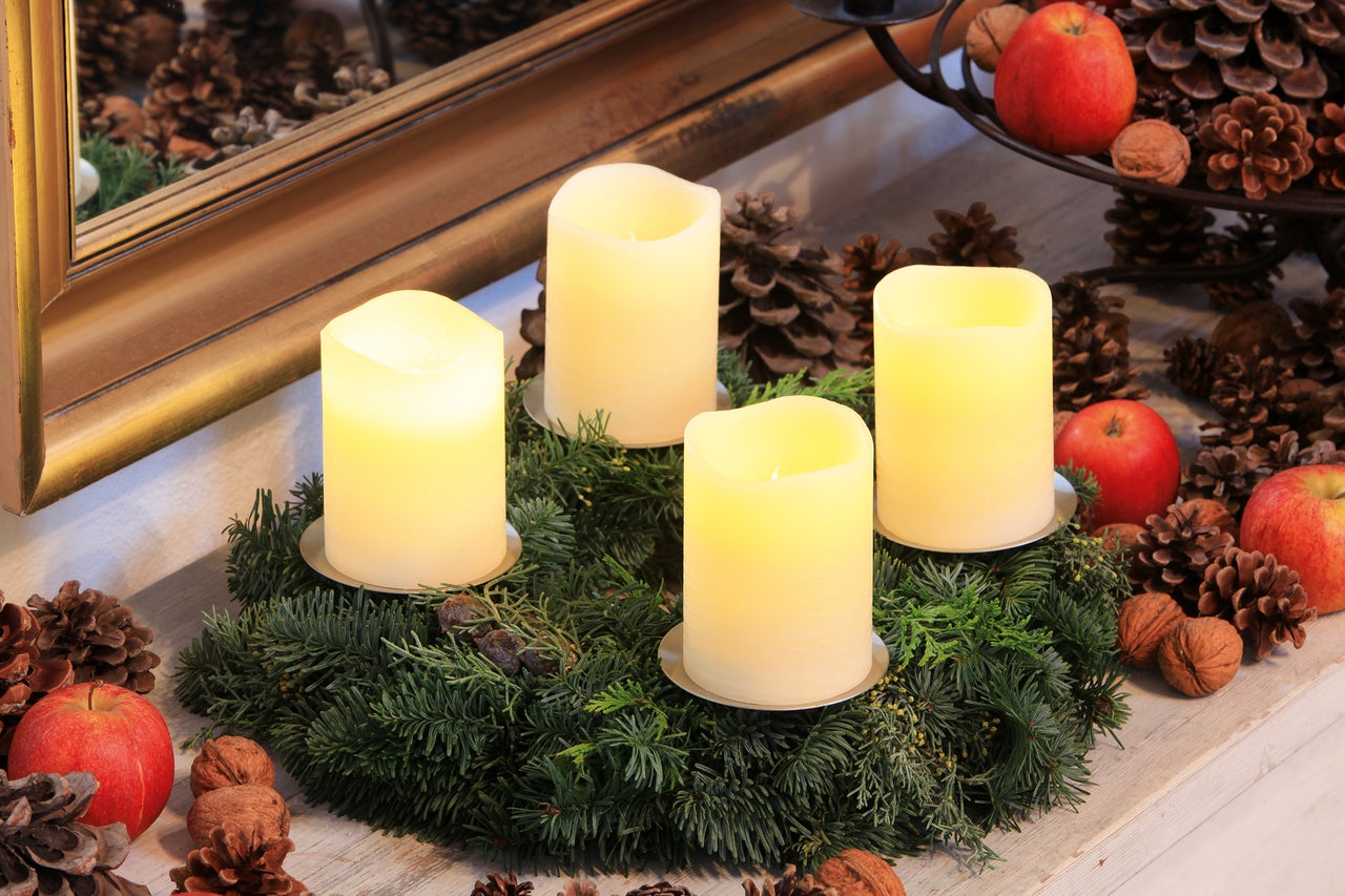 Adventskranz mit vier Kerzen, Tannenzapfen, Äpfeln und Nüssen als festliche Dekoration.