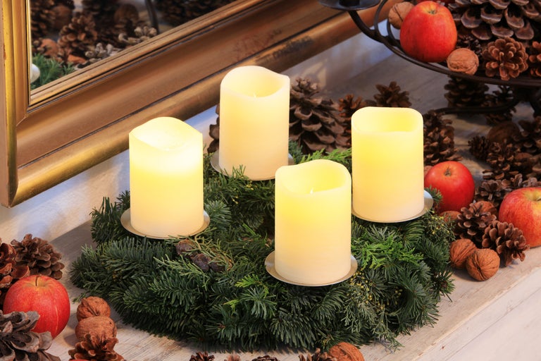 Adventskranz mit vier Kerzen, Tannenzapfen, Äpfeln und Nüssen als festliche Dekoration.