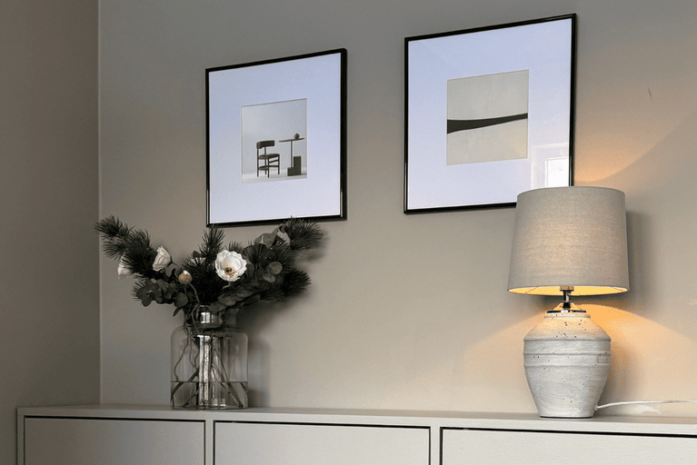 Dekoratives Wohnzimmerambiente mit Tischleuchte, Blumenarrangement und gerahmten Bildern.