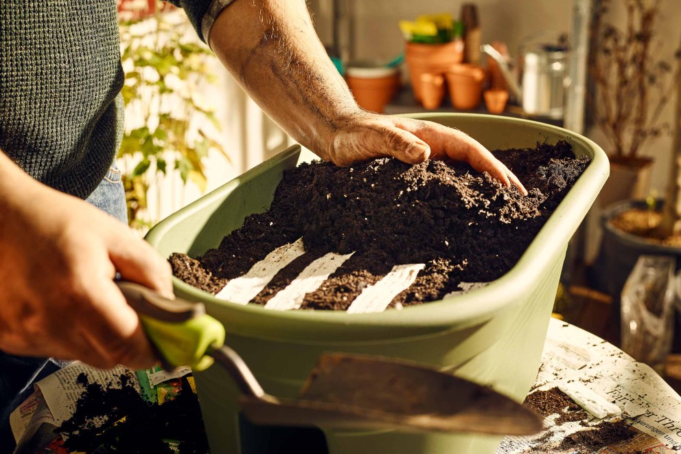 Une personne remplit un bac à plantes avec de la terre et des toiles de semis.