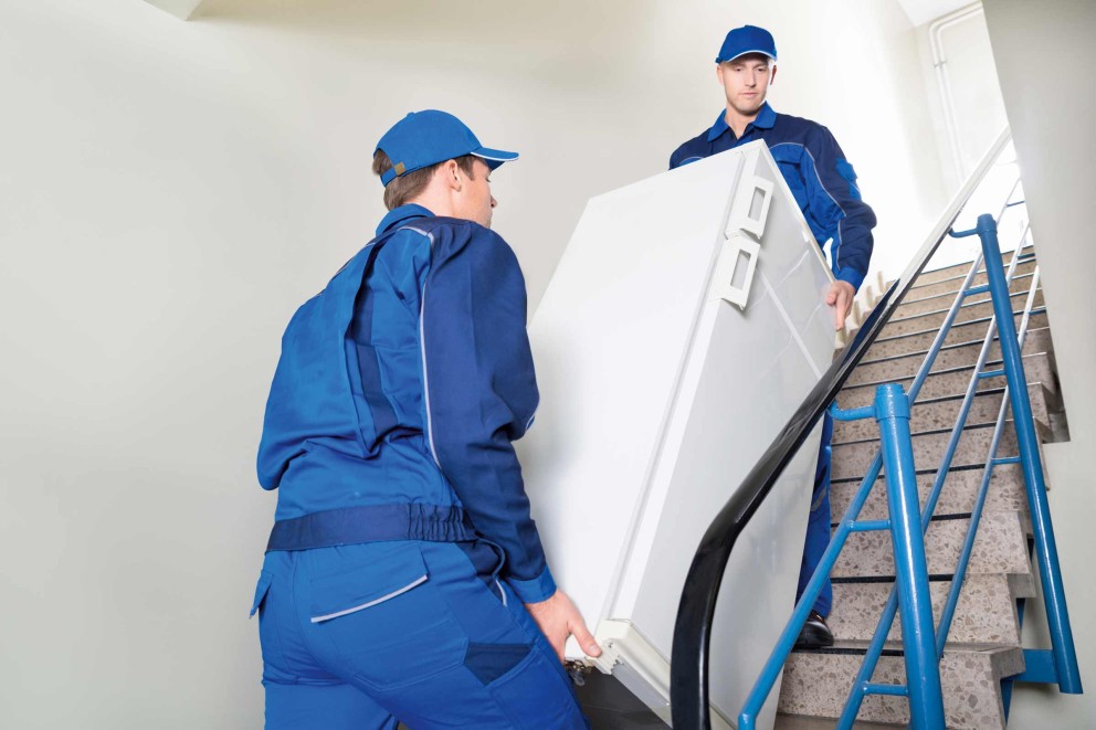 Deux déménageurs montent un réfrigérateur dans l'escalier