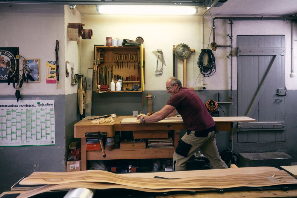 Werkstatt mit Werkbank, Werkzeug und einem Mann, der Holz bearbeitet