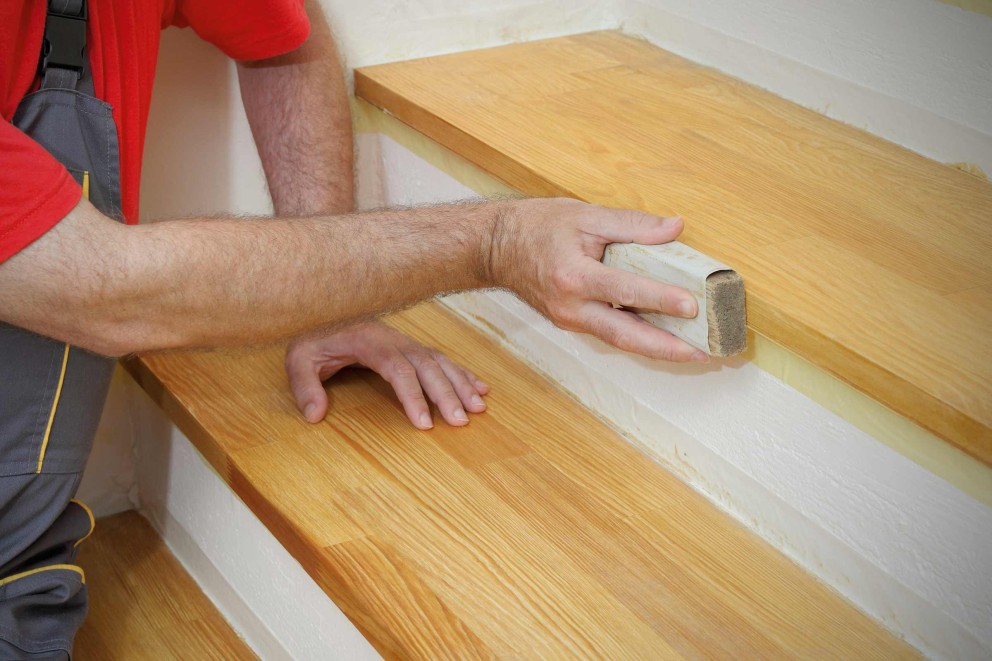 Un homme muni d'un bloc de ponçage sur un escalier avec des marches en bois Un homme muni d'un bloc de ponçage sur un escalier avec des marches en bois