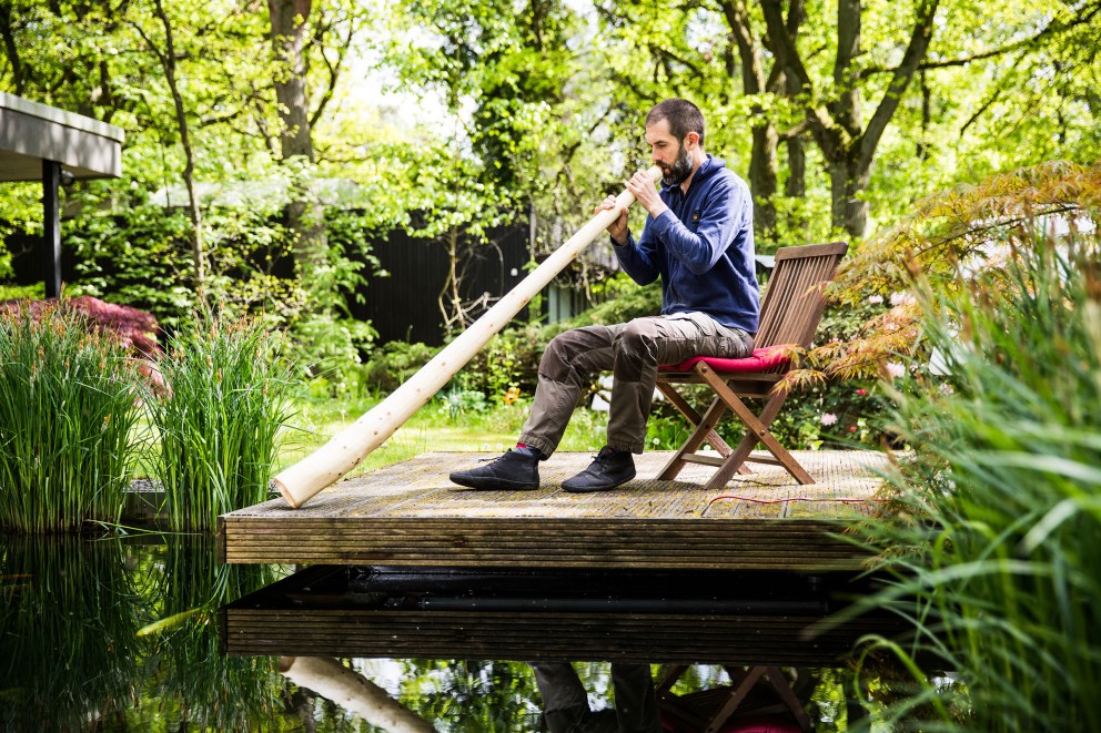 Assis à une table, notre auteur Sascha Borrée souffle dans son didgeridoo Assis à une table, notre auteur Sascha Borrée souffle dans son didgeridoo