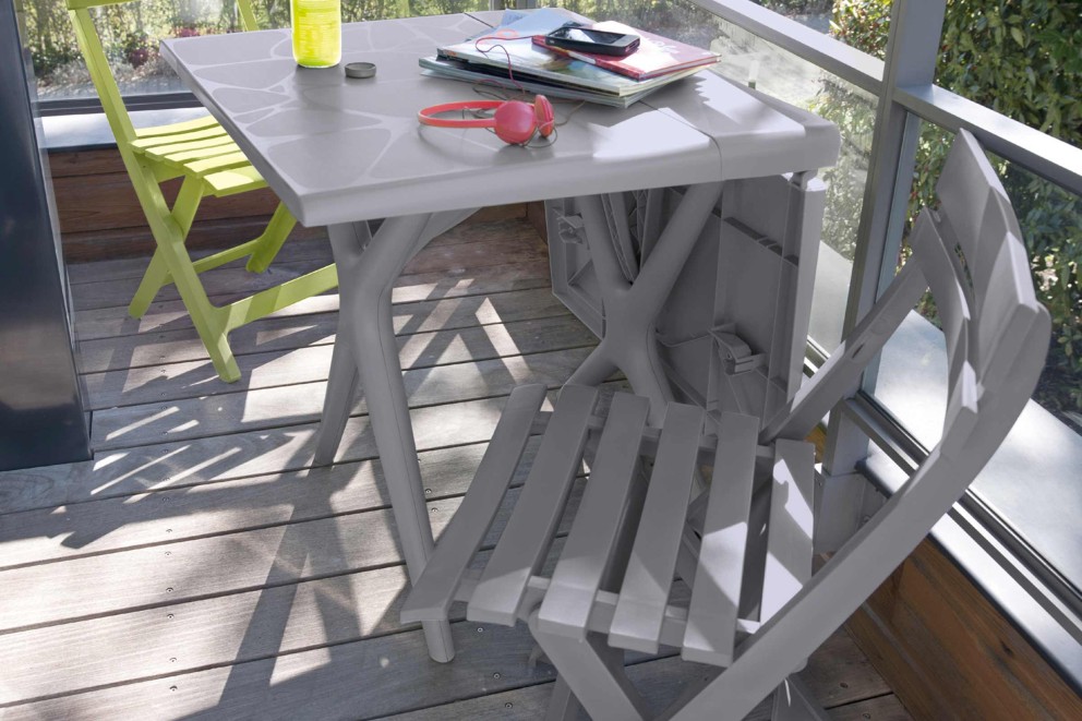 Gartenszene mit grauem Klapptisch, grünem Klappstuhl und Accessoires auf einer Terrasse.