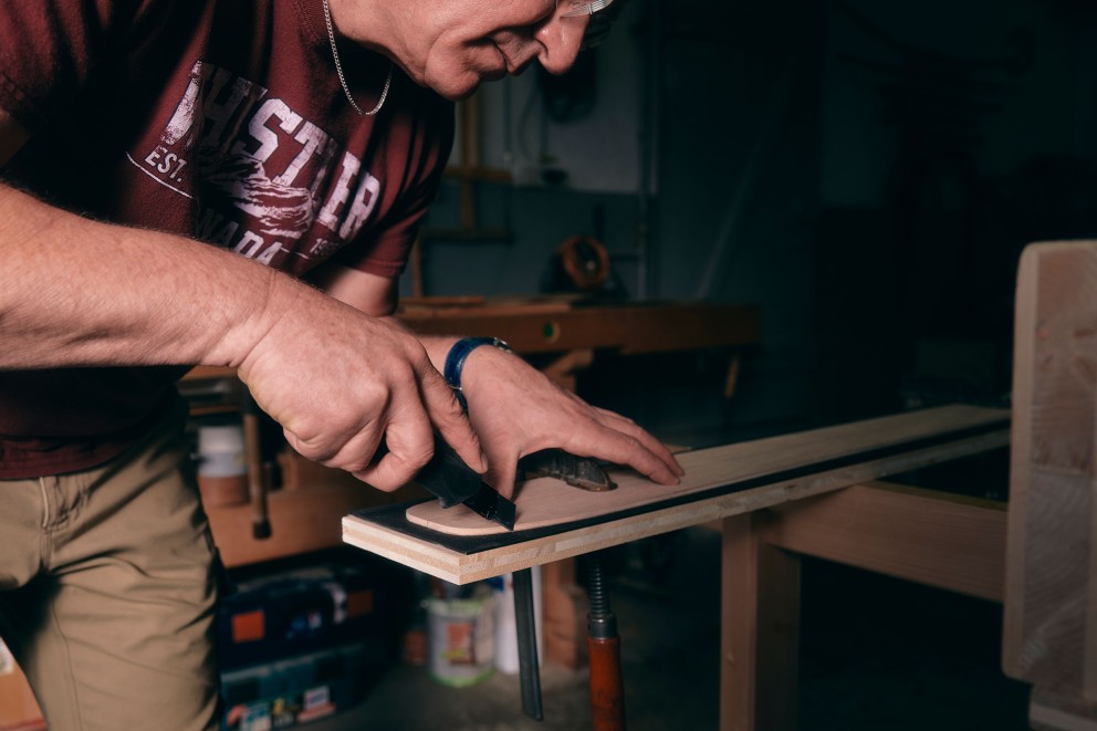 Mann schneidet Holz mit einem Universalmesser auf einer Werkbank
