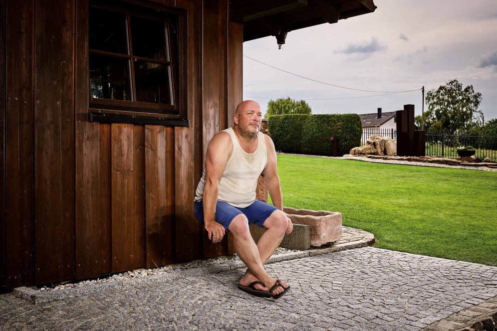 Mann sitzt vor einem Holzhaus im Garten