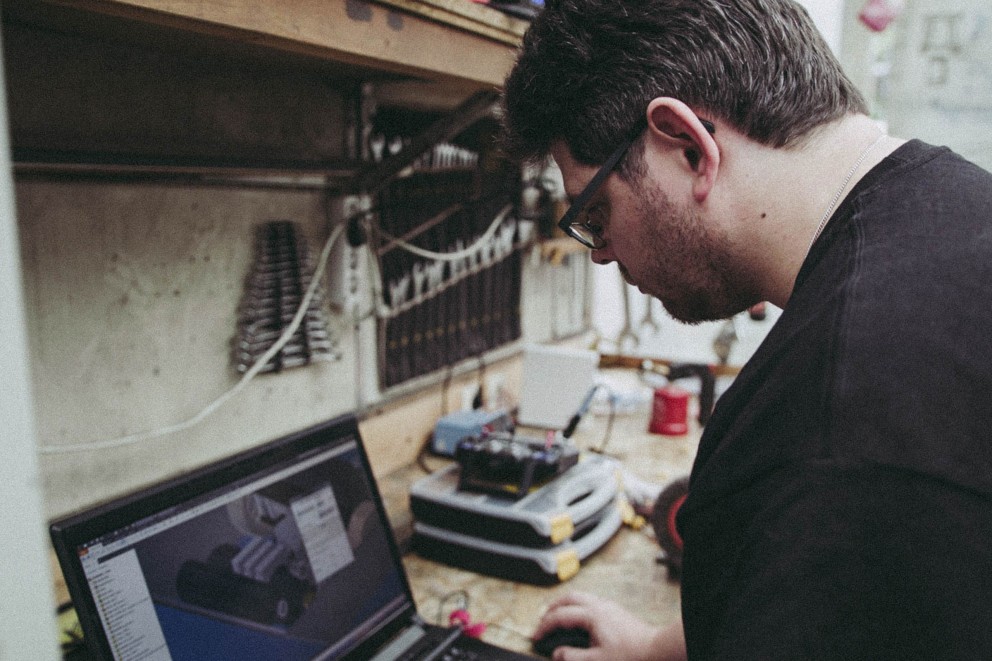 Niels Schotten programmiert einen Roboter an seinem Laptop in der Werkstatt; Niels Schotten programmiert einen Roboter an seinem Laptop in der Werkstatt;