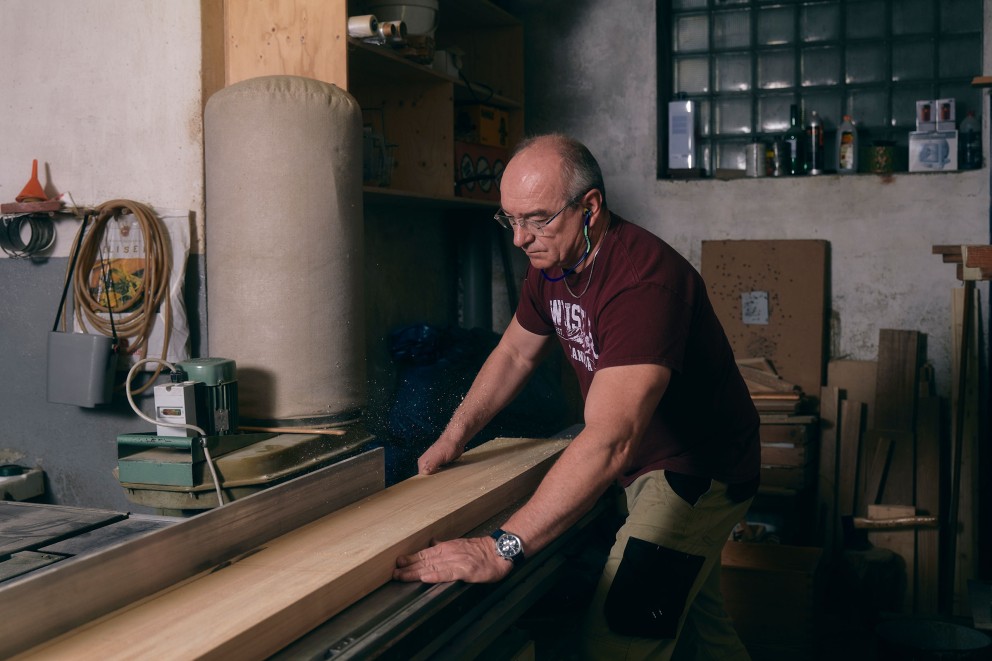 Ein Mann arbeitet mit einer Tischkreissäge an einem Holzbrett in einer Werkstatt.