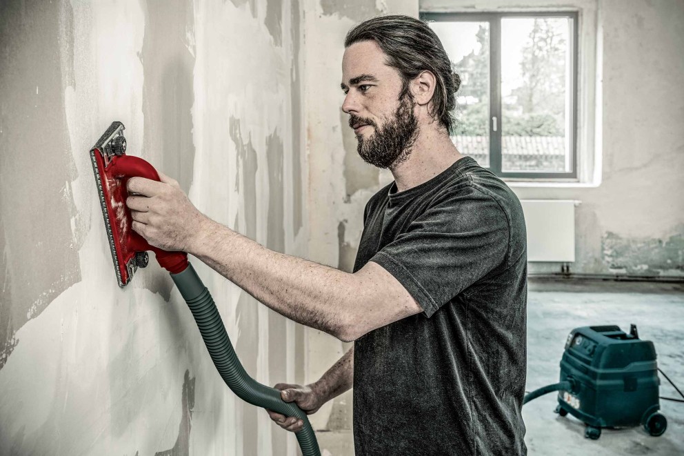 Mann beim Schleifen einer Trockenbauwand mit dem RAUTNER Handschleifer mit Absaugung
