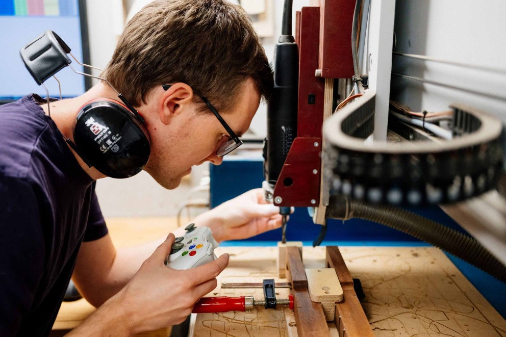 Un homme portant un casque et des lunettes utilise une fraiseuse CNC avec une manette de jeu.