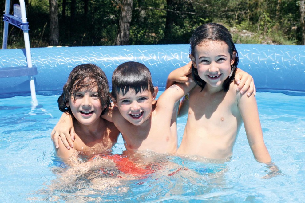 Drei Kinder im hellen Pool mit Leiter im Hintergrund