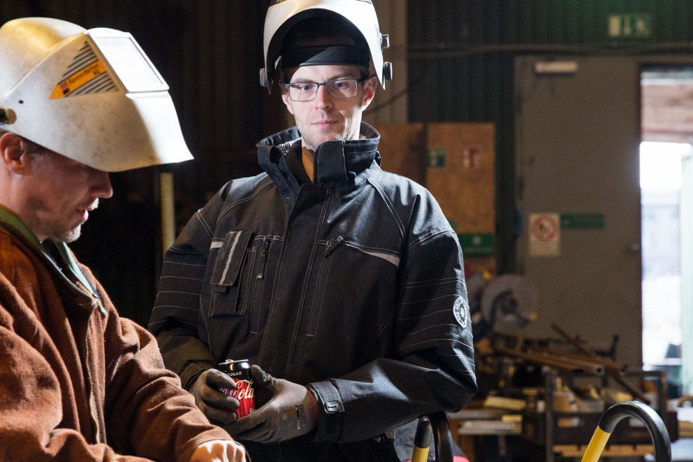 Deux artisans portant des casques de protection et des vêtements de travail dans un atelier.