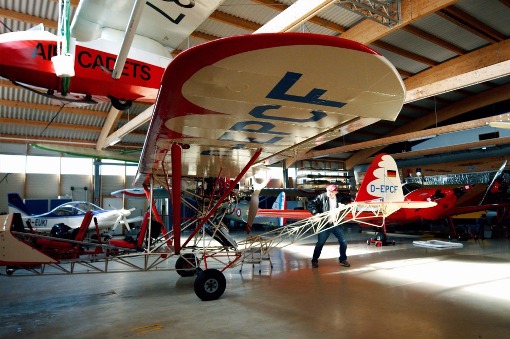 Flugzeughalle mit mehreren Flugzeugen, darunter ein rotes Doppeldeckerflugzeug